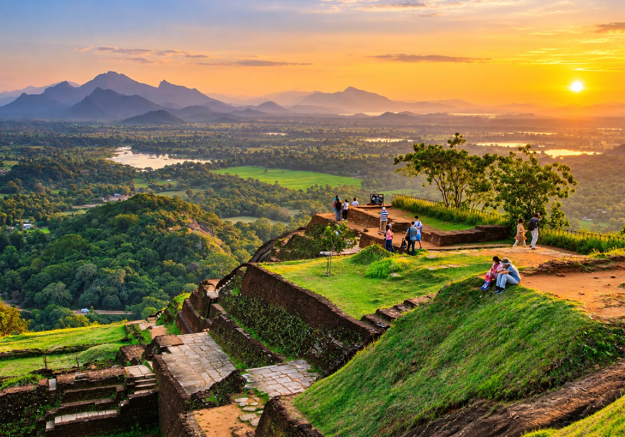Sigiriya Rock Fortress ruins overlooking Sri Lanka’s lush green landscape and distant mountains at sunset.