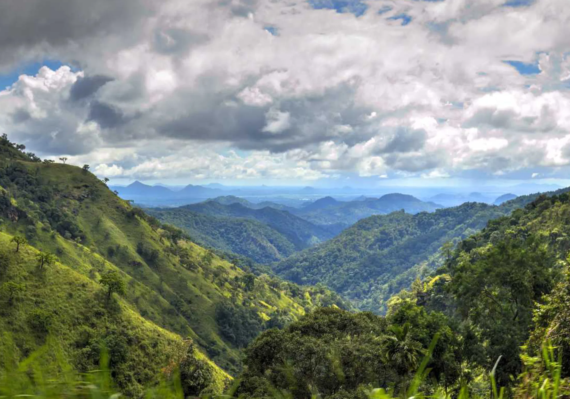 Sri Lanka hill country attractions featuring lush green mountain valleys, forest-covered hills, and scenic landscapes beneath a cloudy blue sky.